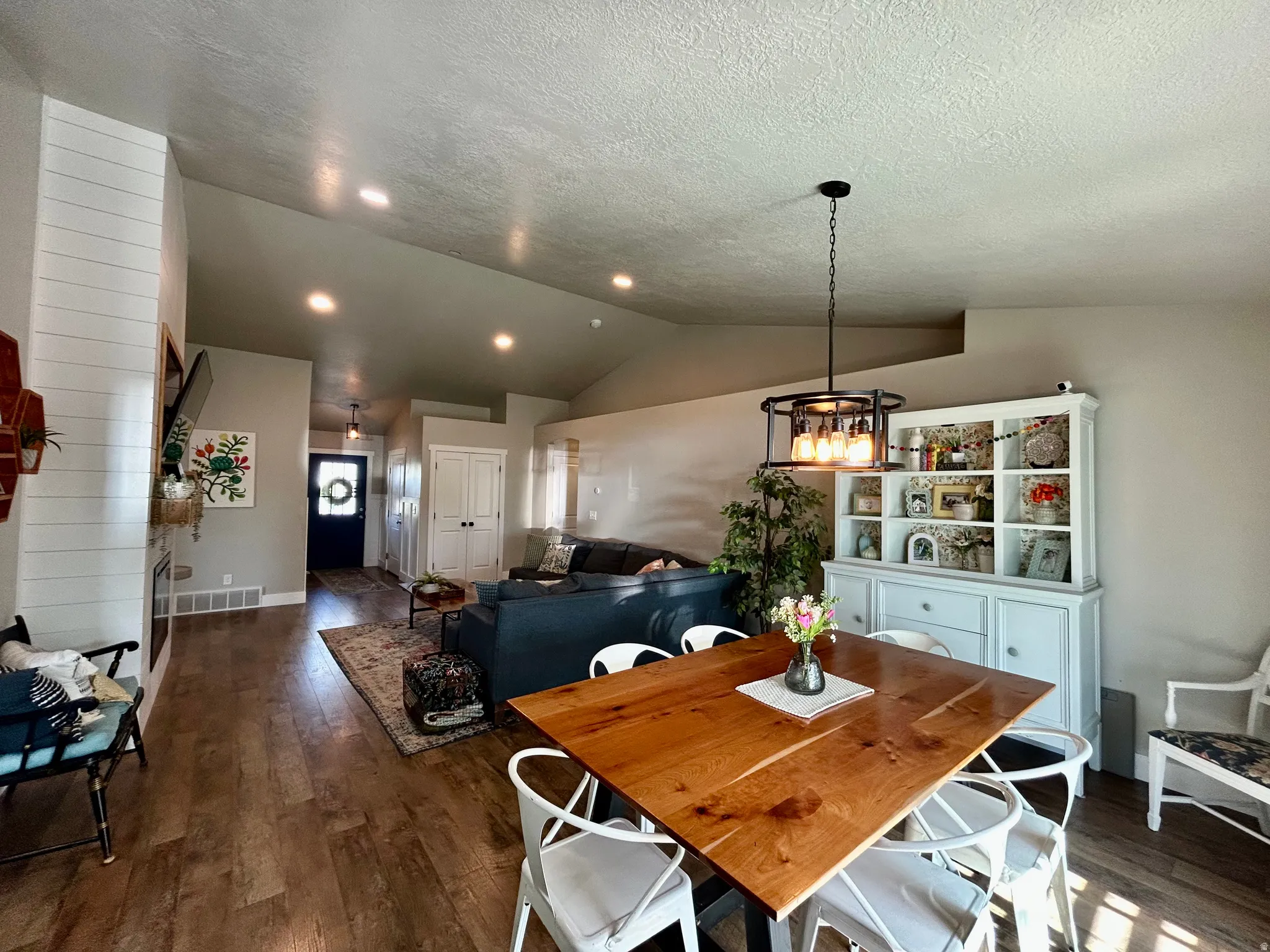 Open-concept living space featuring wood-finish flooring, a shiplap-accented fireplace, and vaulted ceilings with recessed lighting