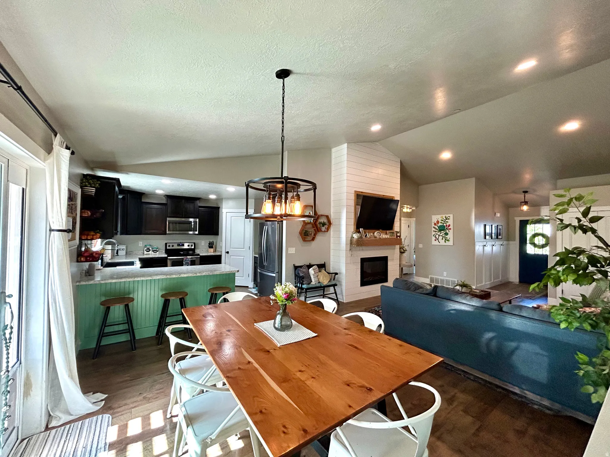 Open-concept living space featuring wood-finish flooring, a contemporary fireplace with shiplap surround, recessed lighting, a kitchen island with beadboard paneling, and dark cabinetry