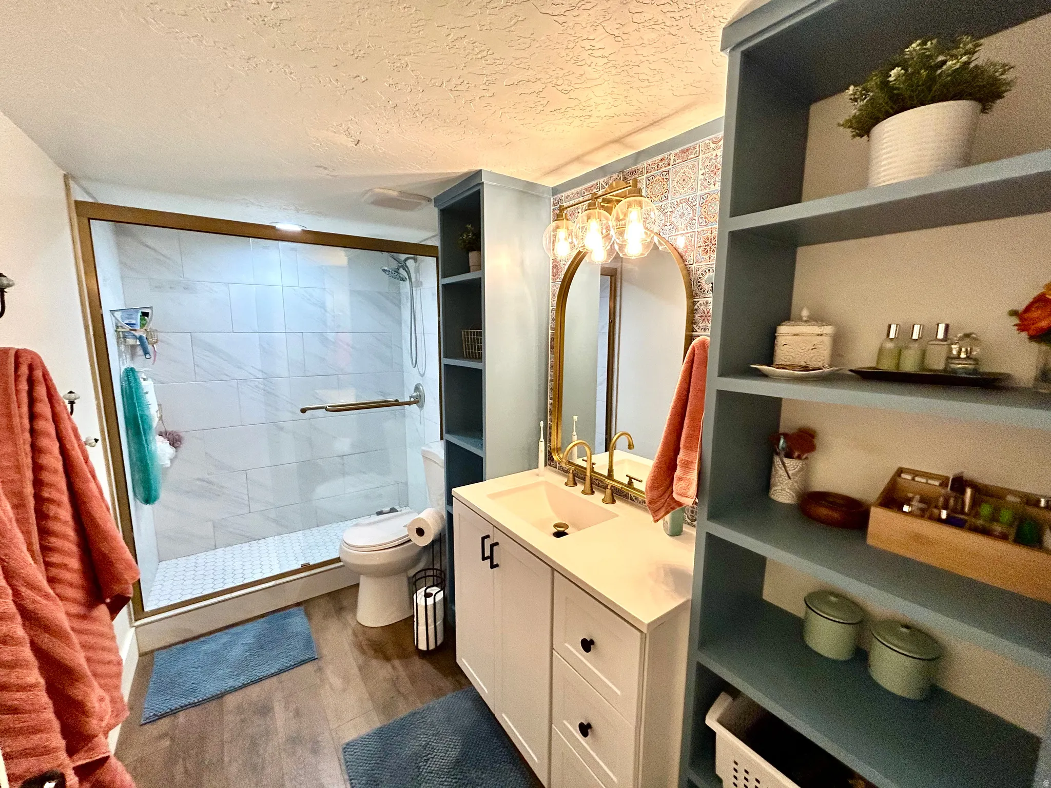 Bathroom featuring a walk-in shower with glass enclosure and white subway tile surround, a white vanity with black hardware, a gold-framed mirror, and wood-finish flooring