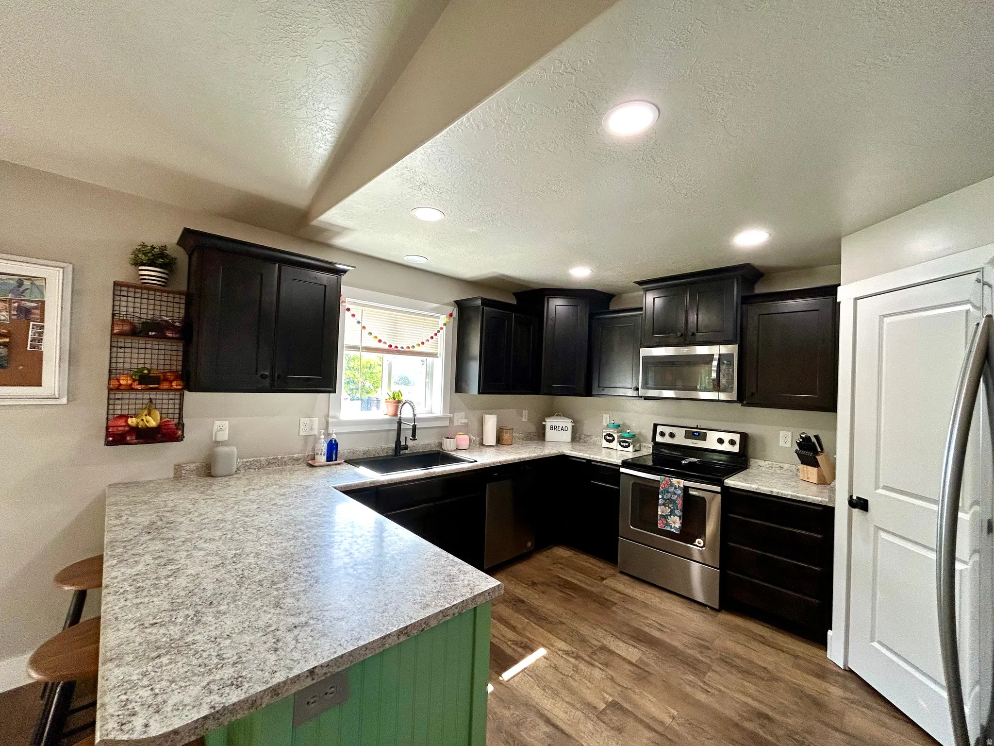 Kitchen featuring wood-finish flooring, dark cabinetry, and light speckled countertops