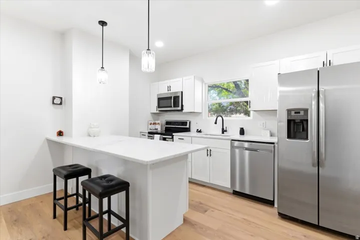 Modern kitchen featuring an eat-at island, stainless steel appliances, white cabinetry, recessed lighting, and wood-finish flooring.