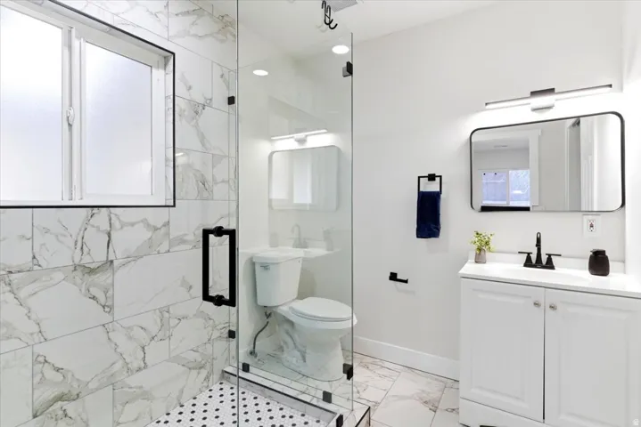 En-suite bathroom featuring a glass-enclosed shower with black hex-tile flooring and marble-look wall tiles