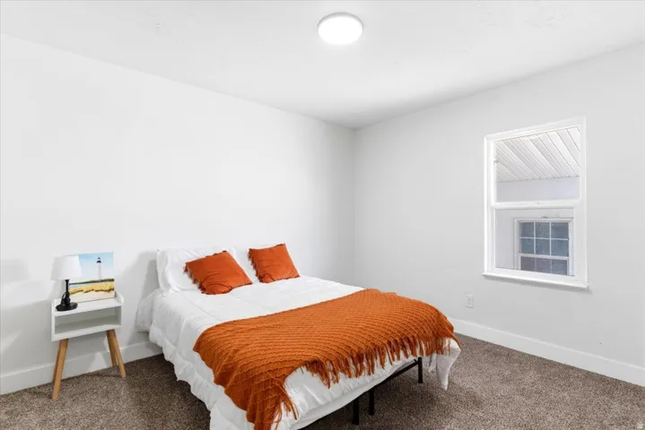 Bright bedroom featuring window, neutral wall tones, and plush carpeting.