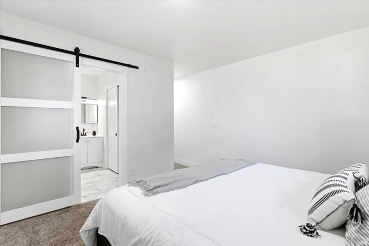 Primary bedroom featuring a white barn door with frosted glass panels, black hardware, and an en-suite bathroom with a white vanity and a rectangular mirror
