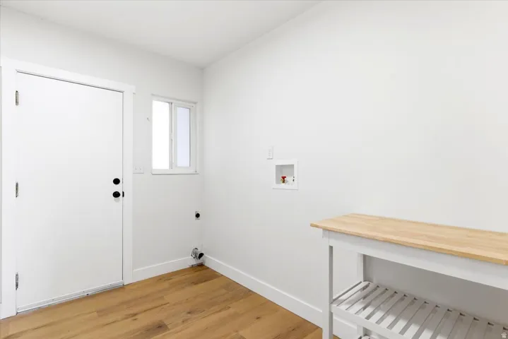Utility room featuring wood-finish flooring, white walls, a single window, and a built-in laundry hookup