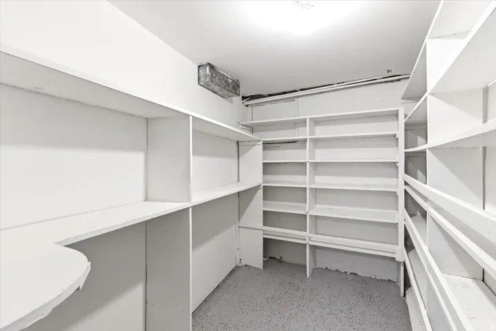 Spacious storage room featuring extensive built-in shelving, durable flooring, a corner counter, and ceiling-mounted lighting