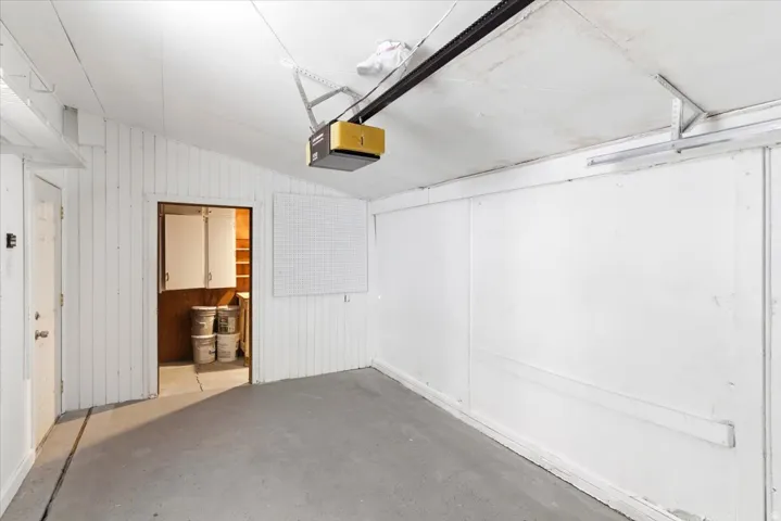 Garage featuring a concrete floor, white paneled walls, a white overhead door, and an interior access door