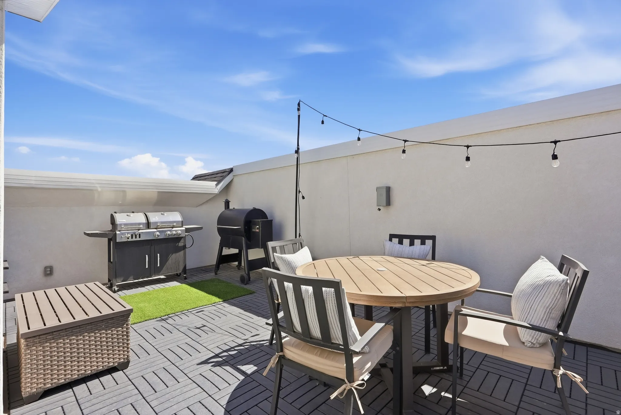 Rooftop patio with interlocking tile flooring, string lighting, and stucco walls