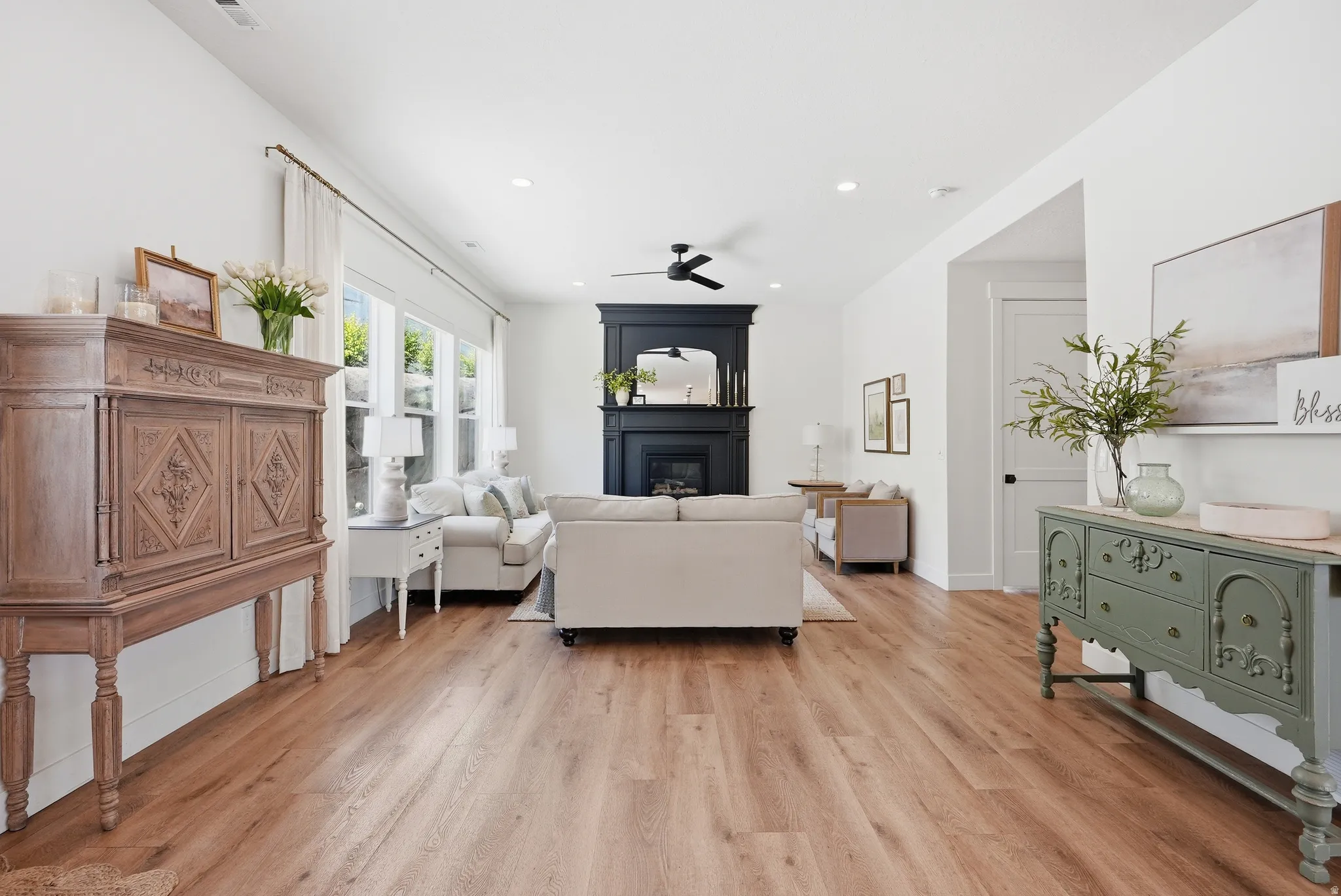Spacious living area featuring LVP flooring, a dark-toned fireplace with mantel, recessed lighting, and large windows with privacy coverings