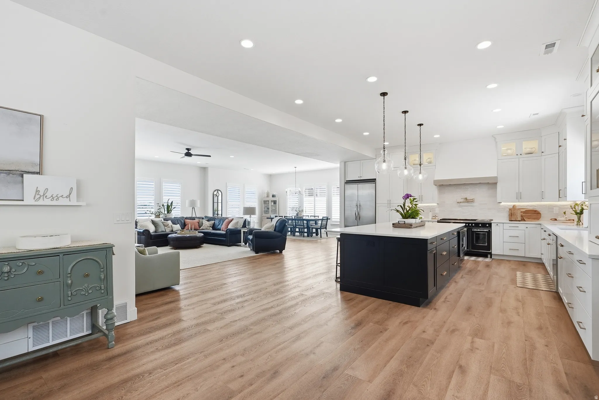 Open-concept living space featuring wood-finish flooring, a contemporary kitchen with a dark-toned island and light-toned cabinetry, stainless steel appliances, and recessed lighting