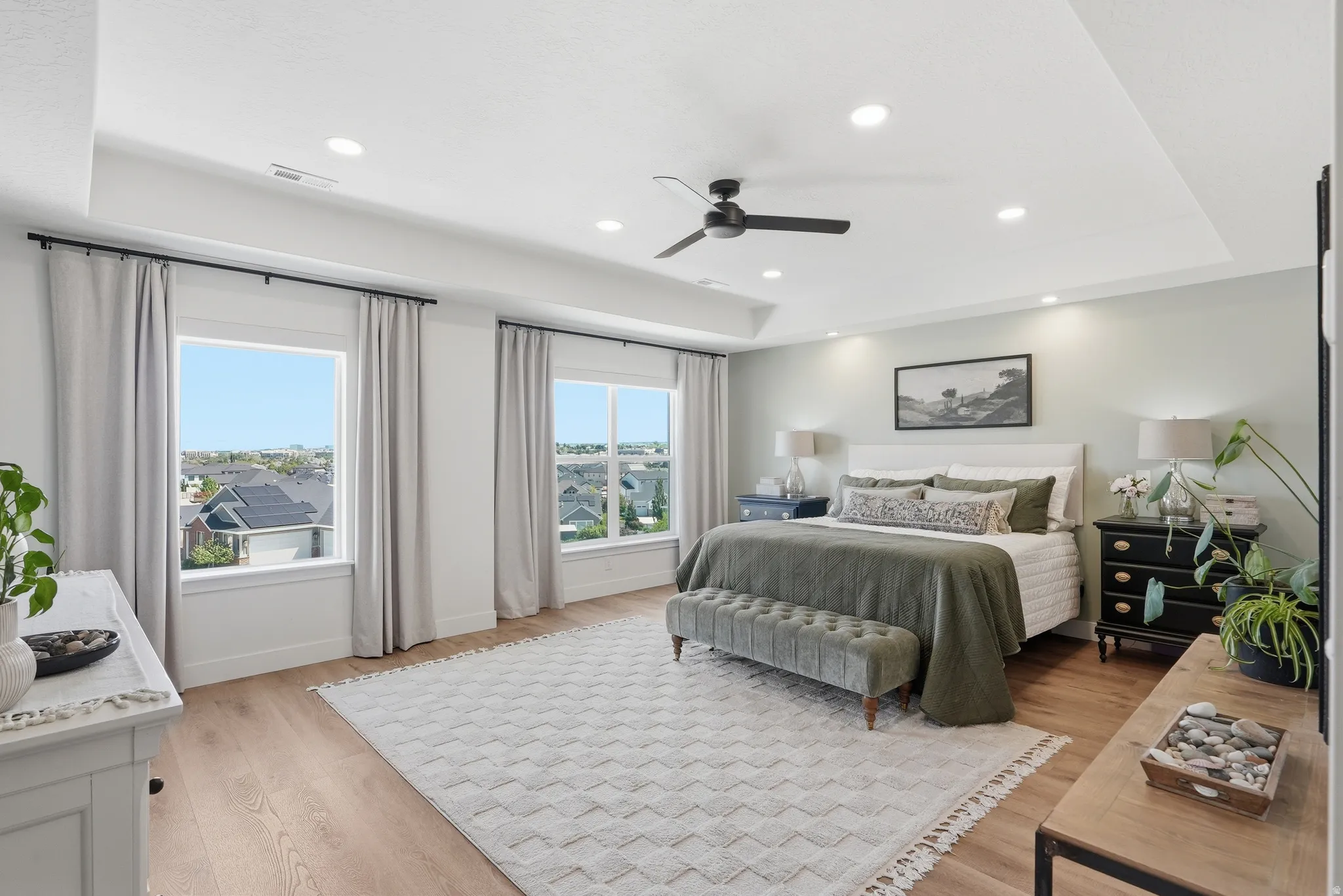 Spacious bedroom featuring warm LVP flooring, a tray ceiling with recessed lighting, and multiple windows