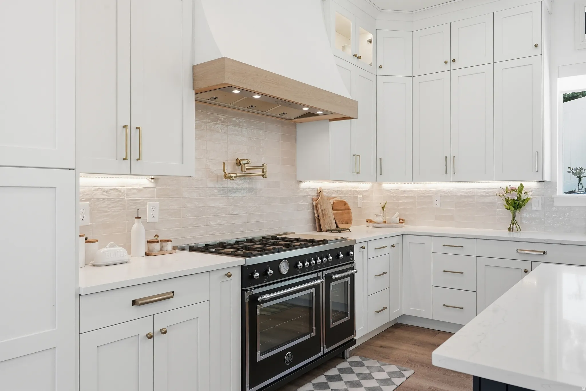 Gourmet kitchen featuring a professional-grade range, pot filler, shaker cabinetry with brass hardware, undermount lighting, and quartz countertops
