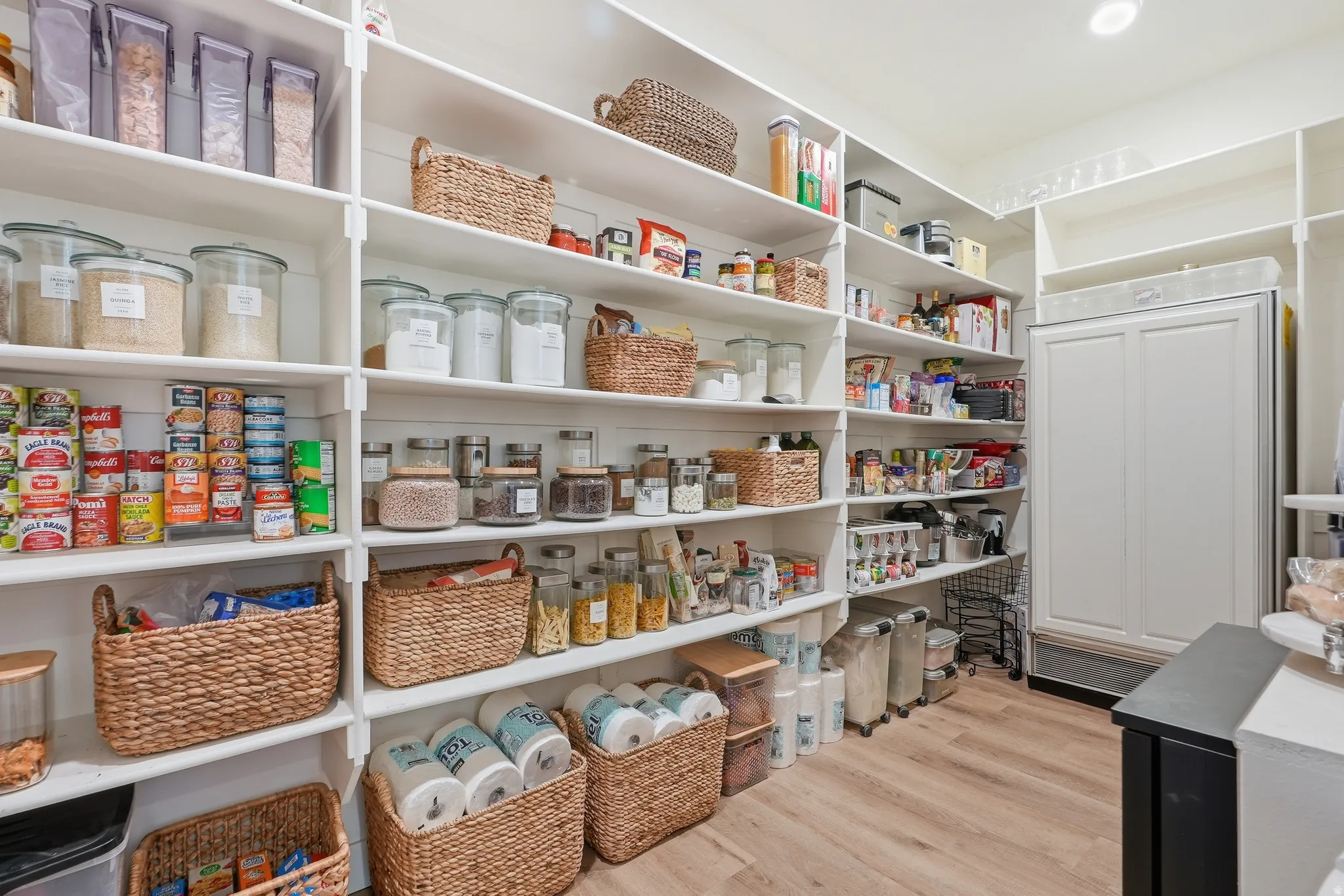 Hidden spacious walk-in pantry featuring extensive built-in shelving, LVP flooring, recessed lighting, and a built-in cabinet