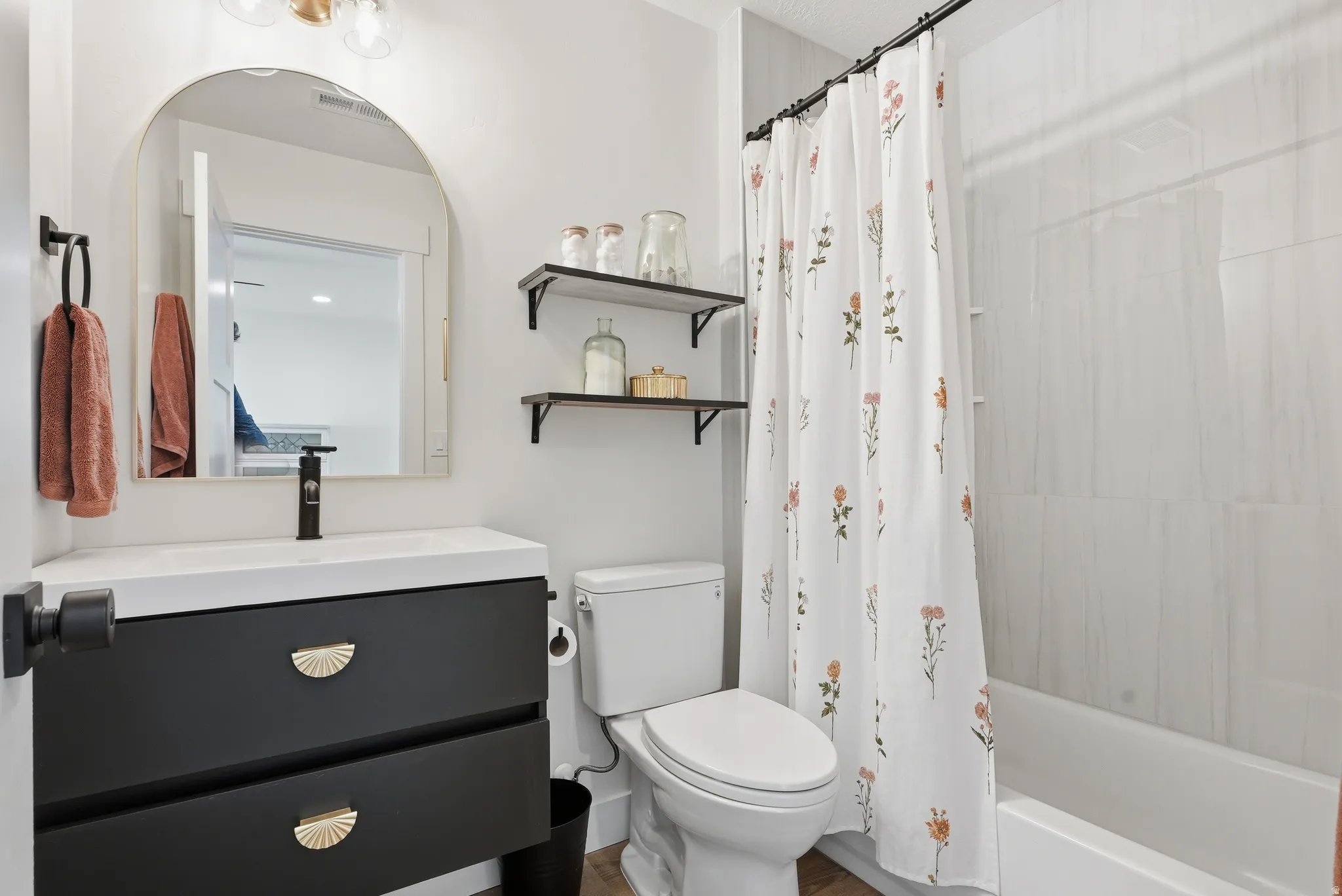 Modern bathroom featuring a dark vanity with gold hardware, white countertop, and a contemporary arched mirror