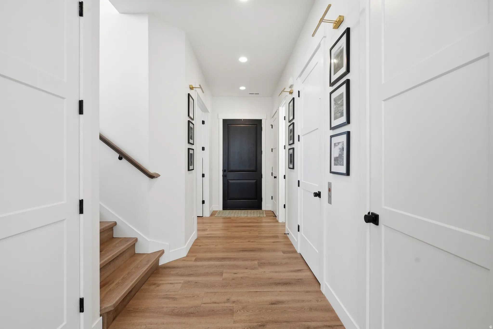 Bright hallway featuring LVP flooring, recessed lighting, and a dark paneled door