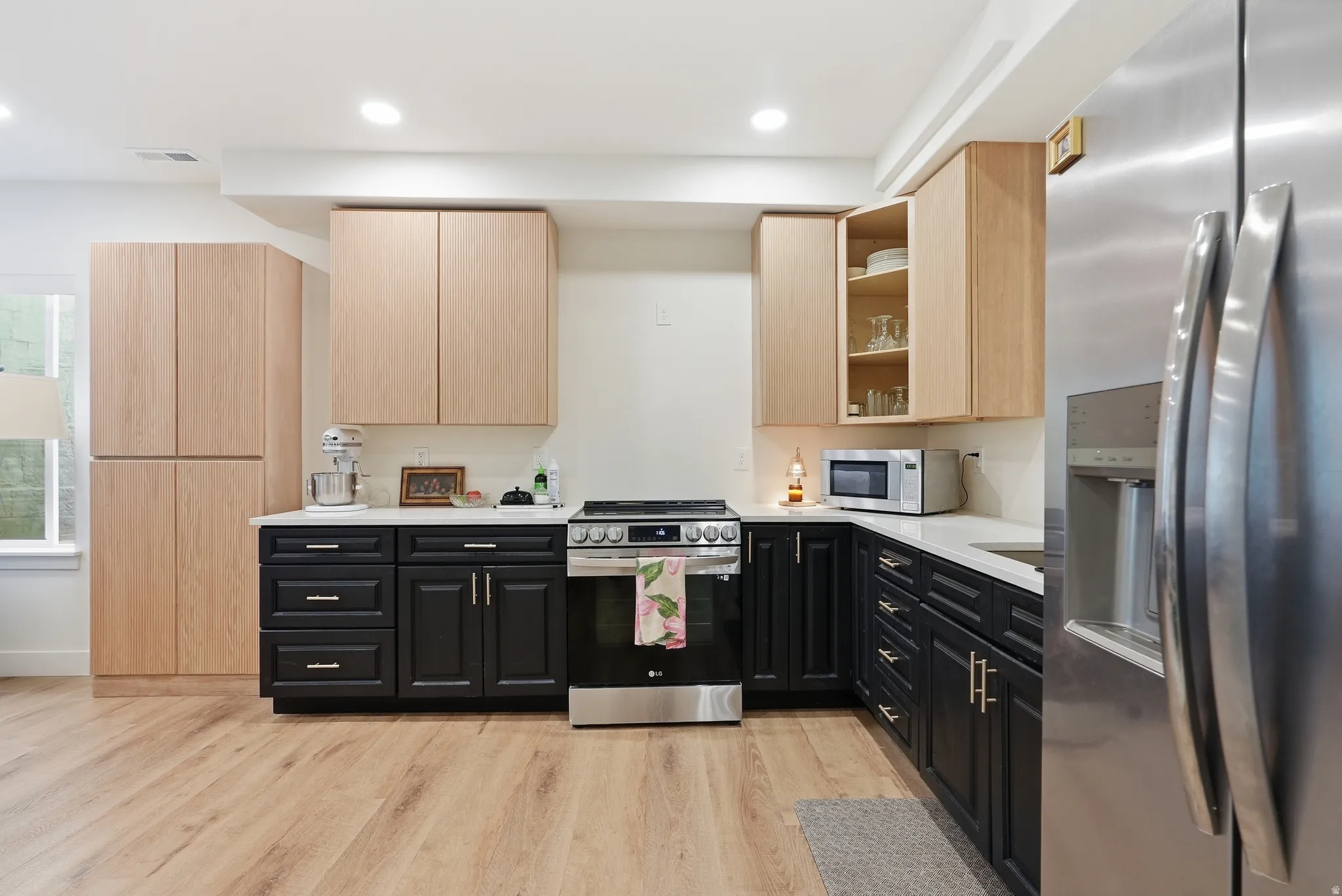 Modern kitchen featuring LVP flooring, two-tone cabinetry with black base cabinets and natural wood upper cabinets, a stainless steel refrigerator, and recessed lighting