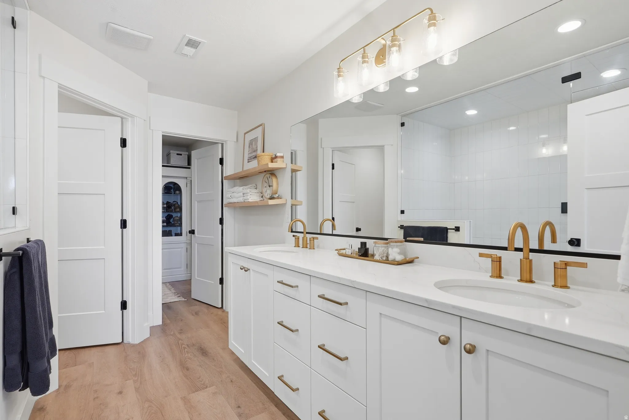 White double vanity with brass hardware and fixtures, quartz countertops, and a large integrated mirror