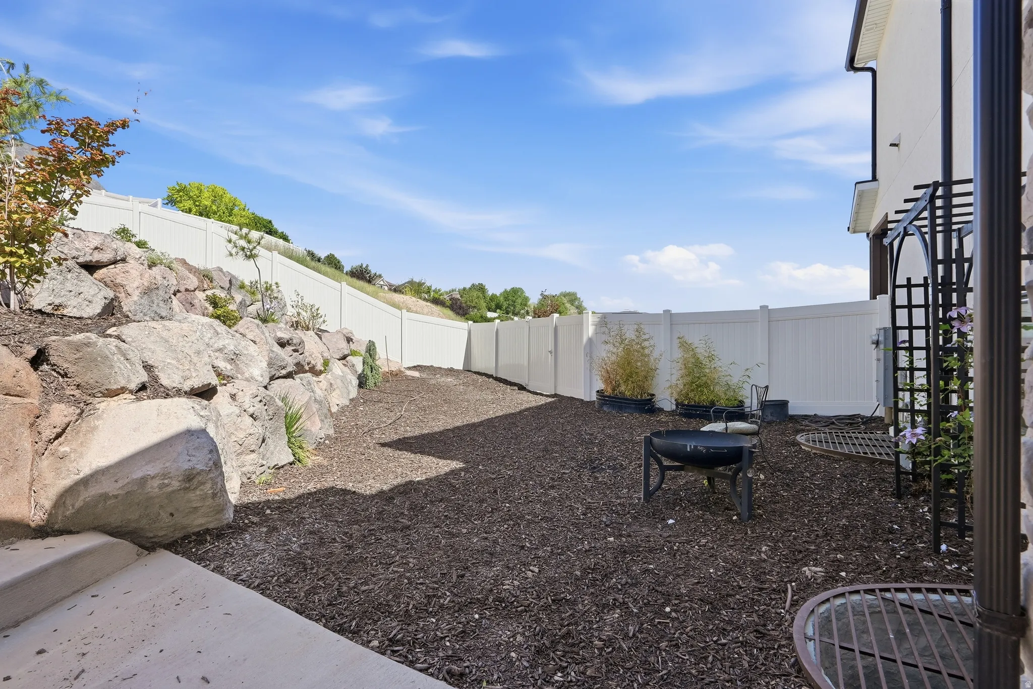 Expansive backyard area featuring a rock retaining wall, privacy fencing, and wood chip ground cover
