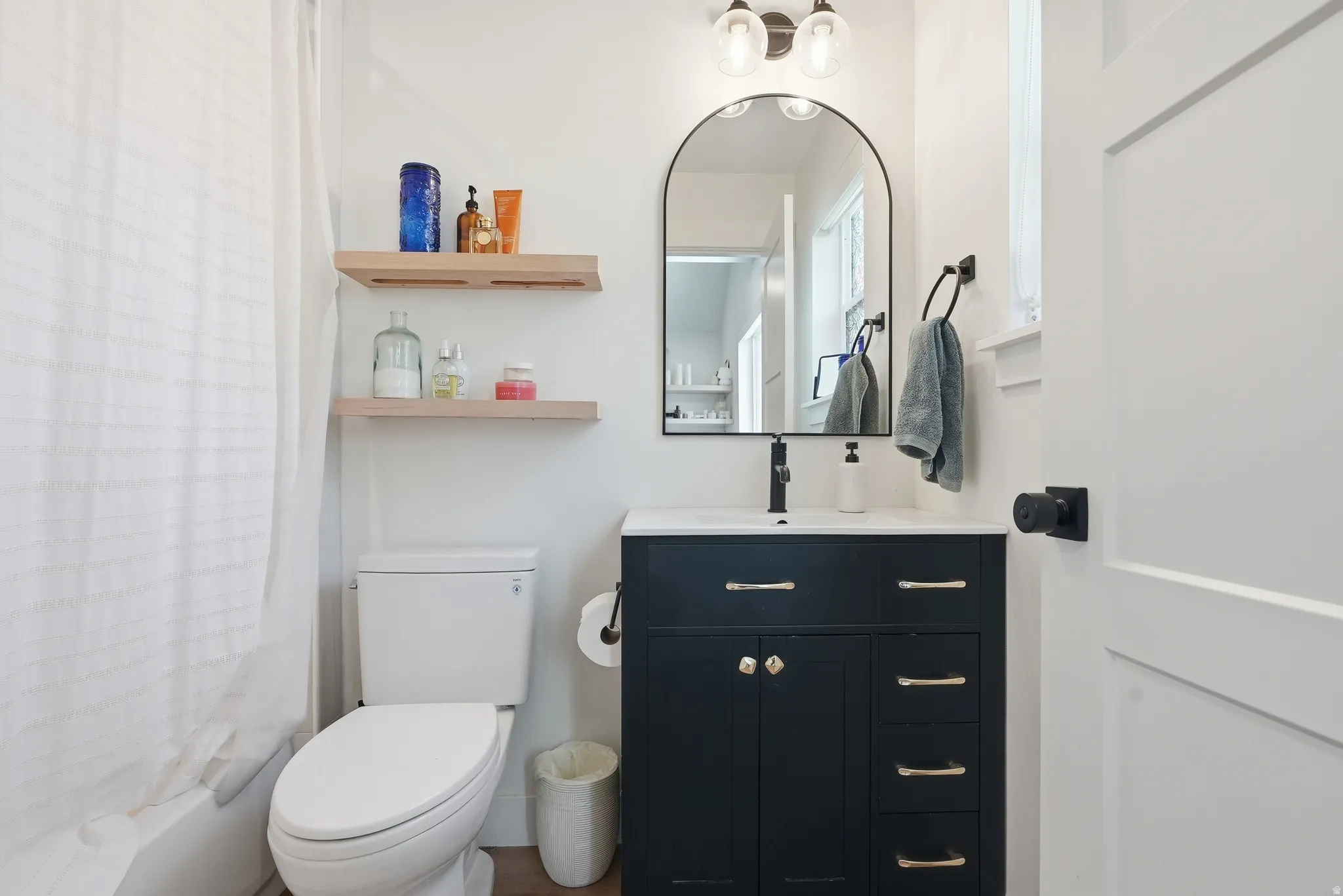 Bathroom featuring a dark blue vanity with gold hardware, a white countertop, and a black-framed arched mirror