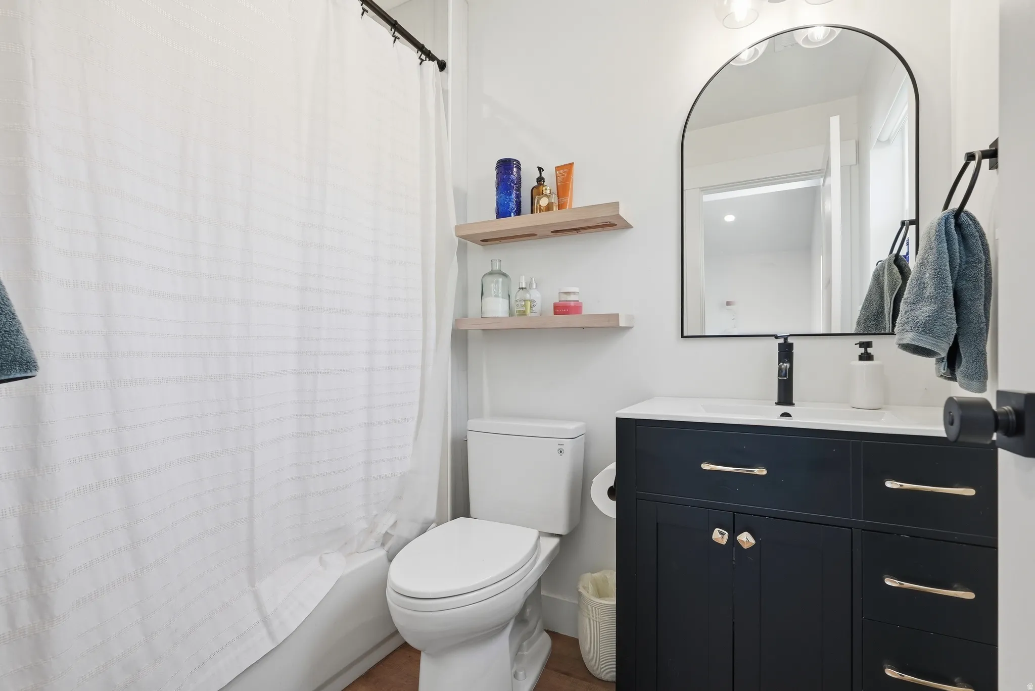 Bathroom featuring a dark vanity with gold hardware, a white integrated sink, and a black wall-mounted faucet