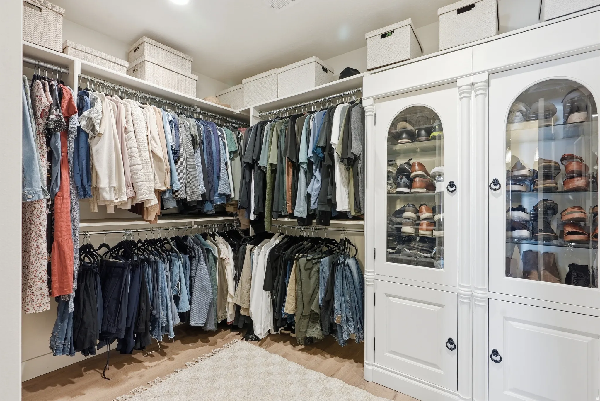 Custom walk-in closet featuring built-in cabinetry with arched glass display doors, multiple clothing rods, integrated shelving, and recessed lighting