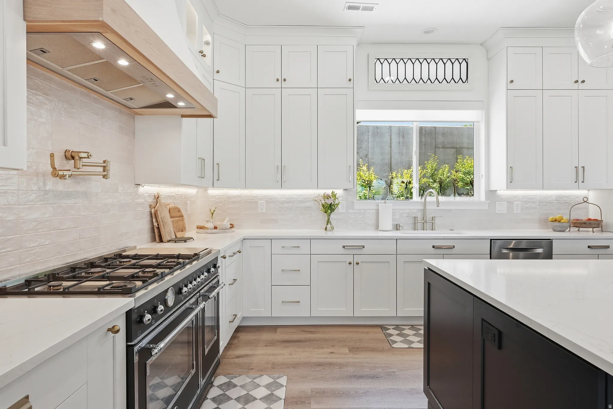 Gourmet kitchen featuring white shaker cabinetry, quartz countertops, wood-finish flooring, a commercial-style range with a pot filler, and a contrasting island with integrated power