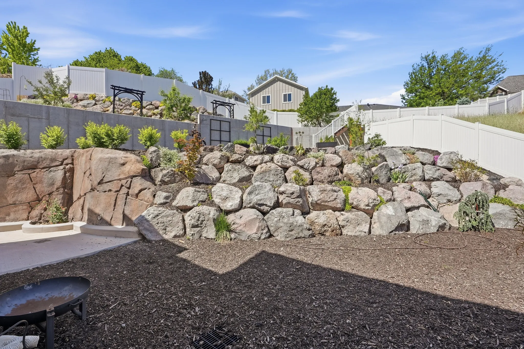 Terraced backyard featuring a natural rock retaining wall, concrete patio, and a dedicated planting area with established shrubs