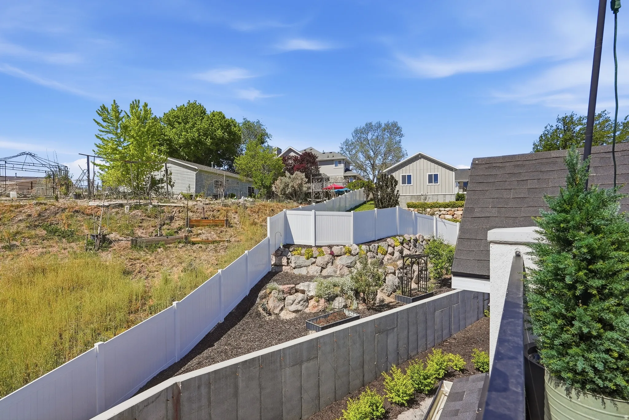 Terraced landscaping featuring a white vinyl privacy fence, rock retaining wall, and planted shrubs