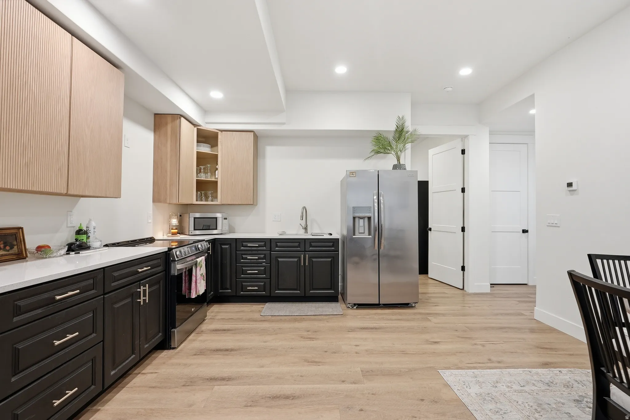 Modern kitchen featuring a stainless steel refrigerator, black base cabinetry, wood-finish upper cabinetry, quartz countertops, and wLVP flooring