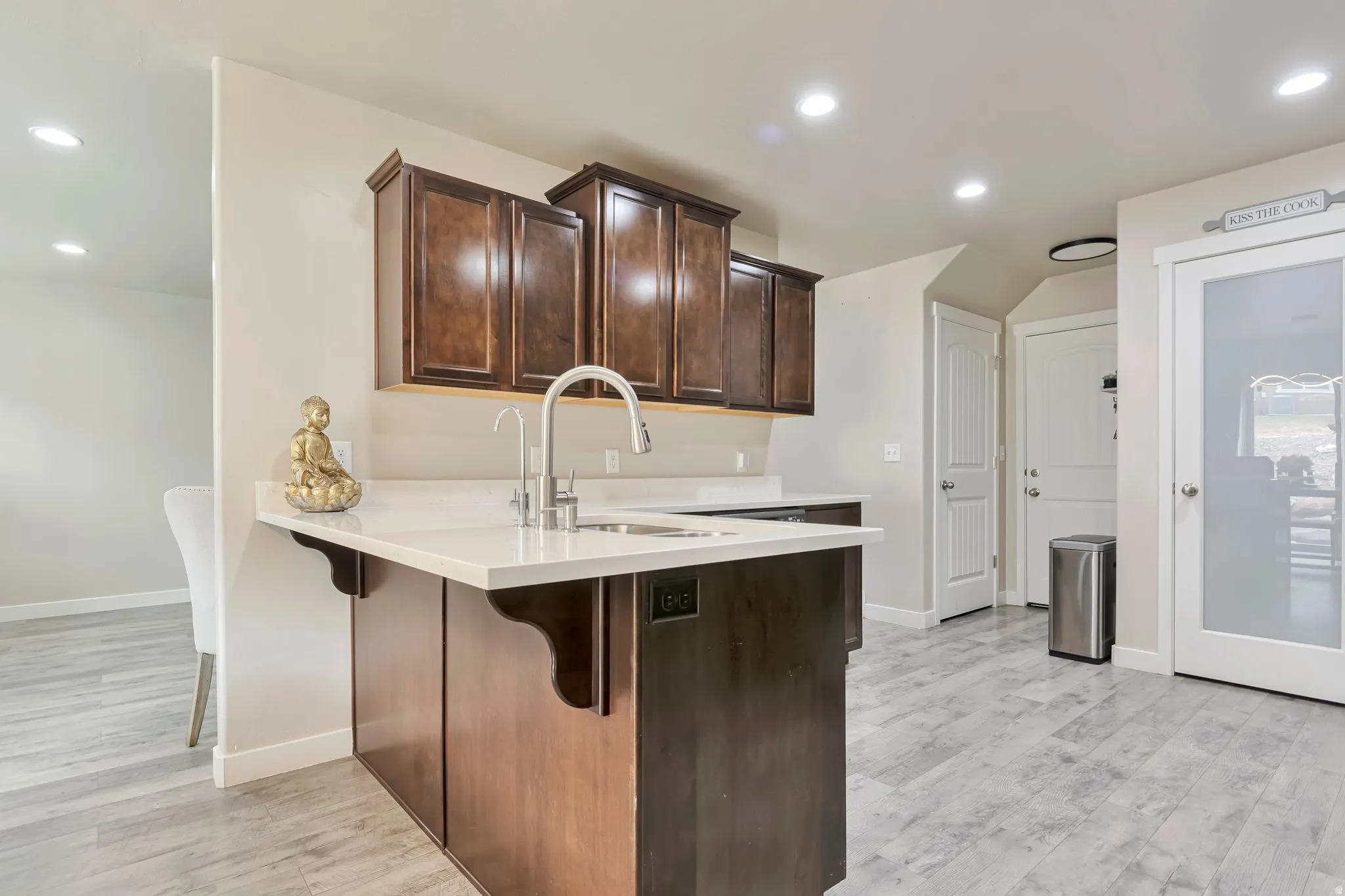 Kitchen island featuring a double basin sink with a gooseneck faucet, light-toned countertop, and dark wood-finish cabinetry