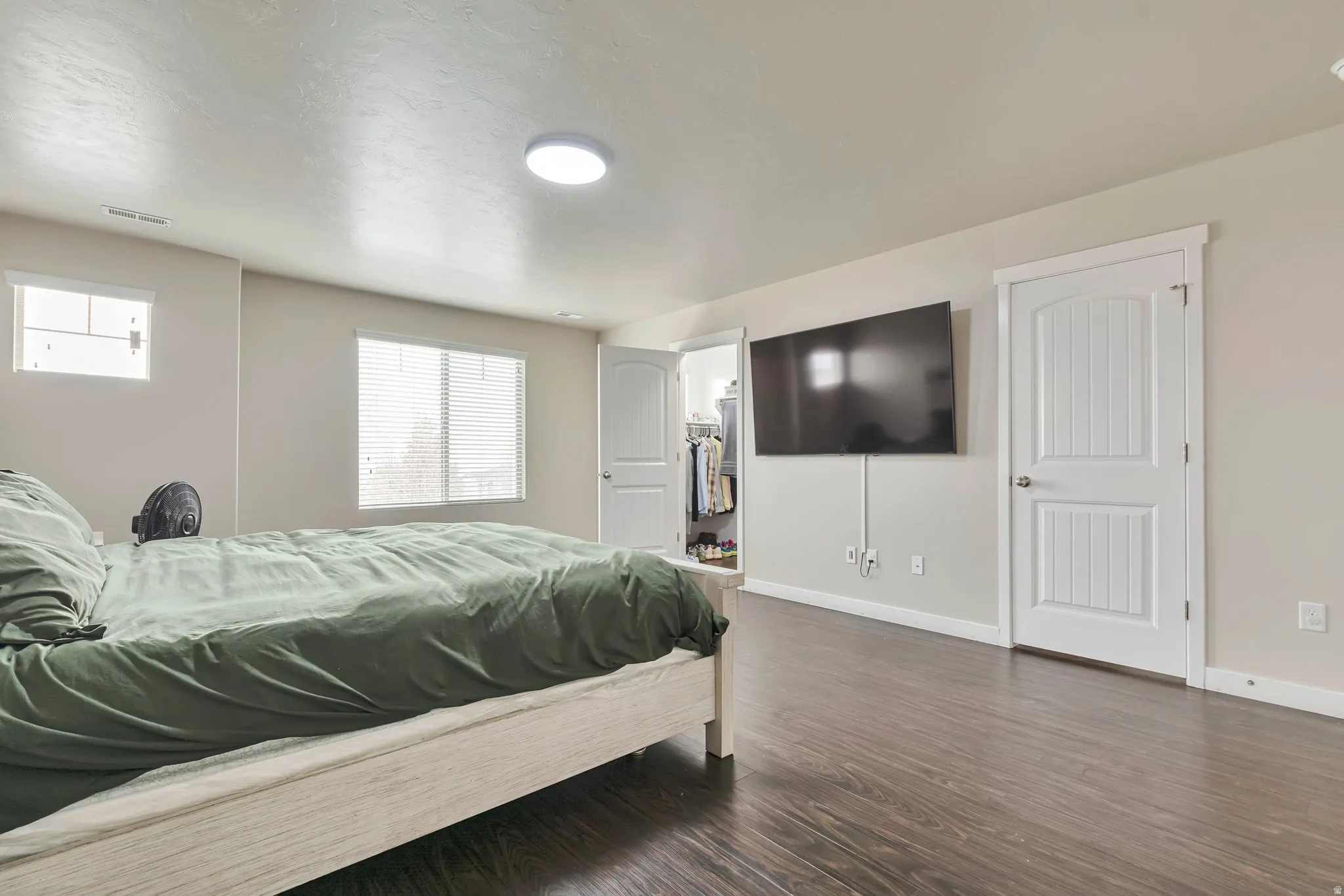 Spacious room featuring dark wood-finish flooring, light-toned walls, and multiple windows with blinds