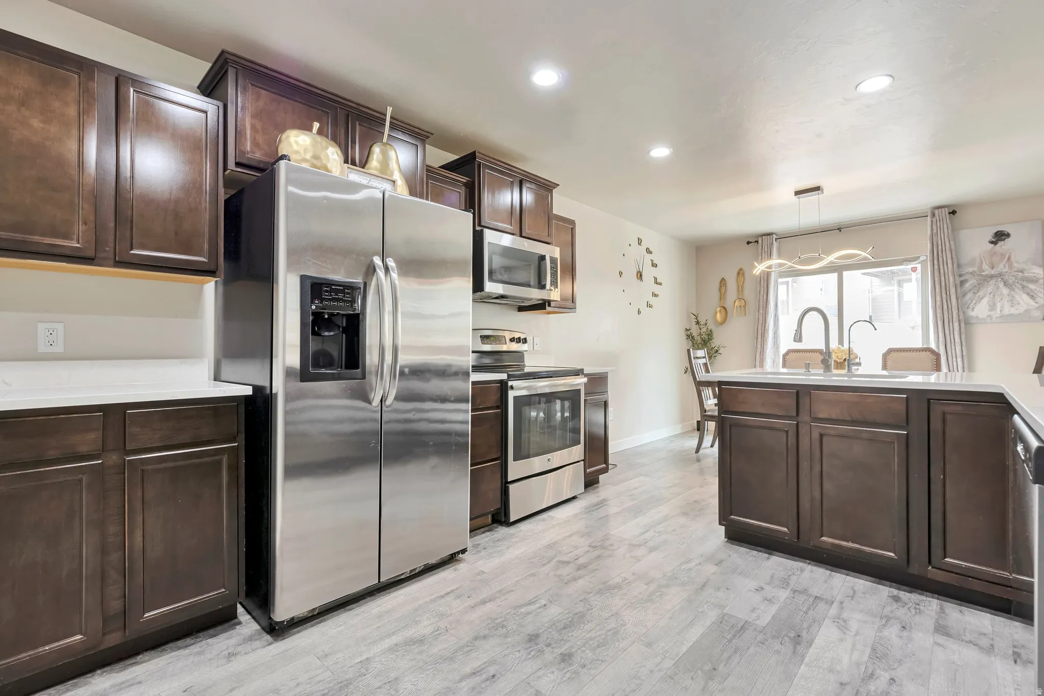 Modern kitchen featuring wood-finish flooring, dark wood cabinetry, white countertops, and stainless steel appliances