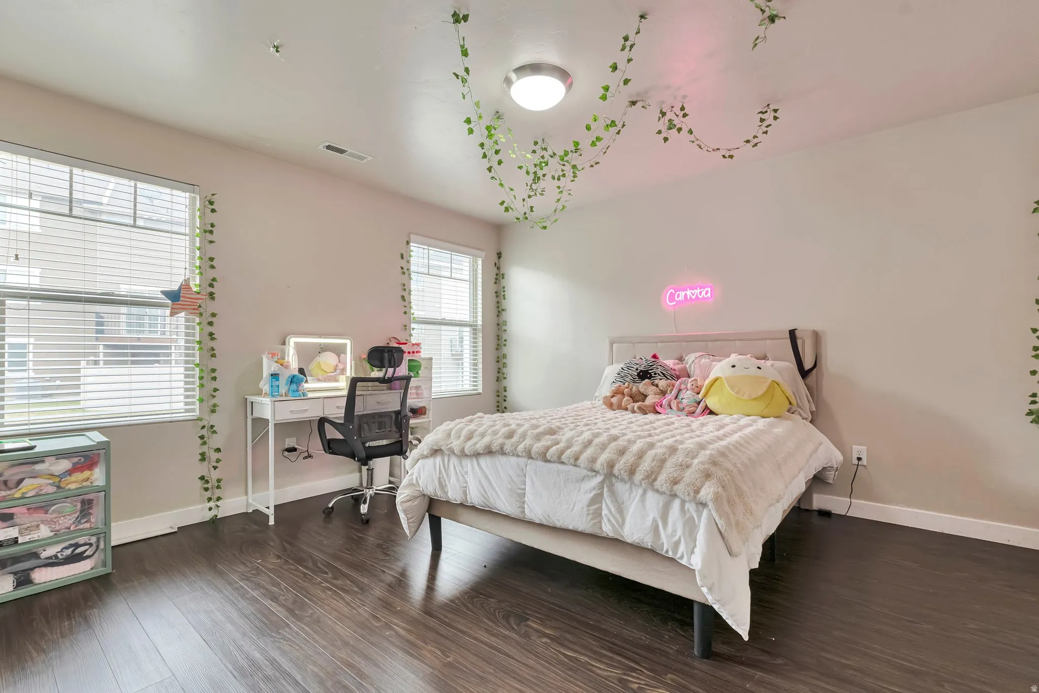 Spacious room featuring wood-finish flooring, two large windows with blinds, and a neutral wall color