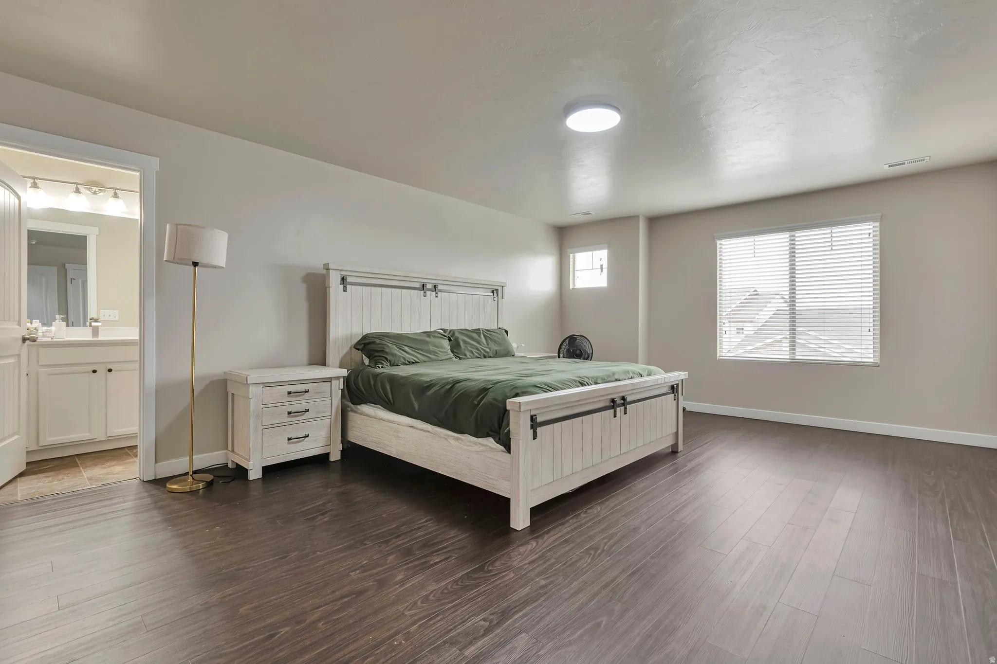 Spacious room featuring dark wood-finish flooring, light neutral walls, and a large window with blinds