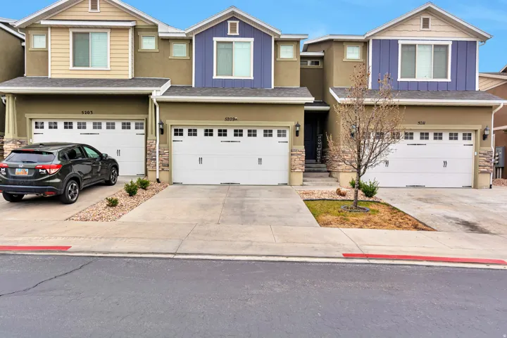 Townhome exterior featuring tan stucco siding, contrasting blue and beige facade accents, white garage doors with window inserts, and stone veneer columns