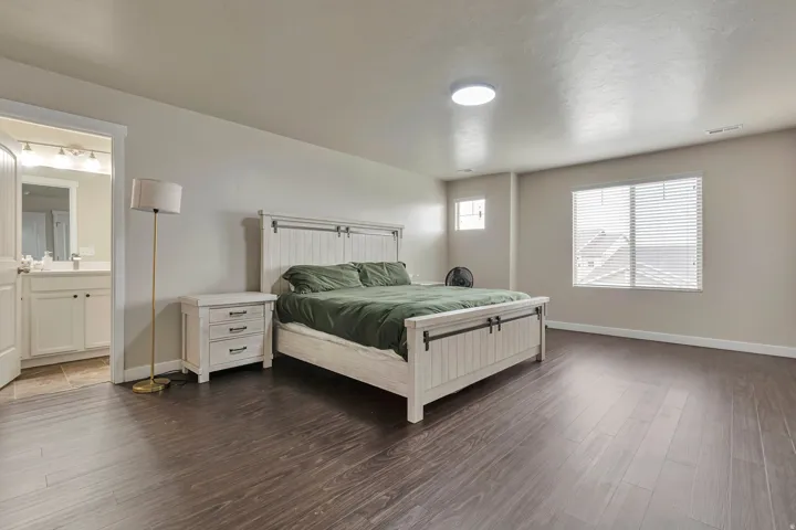 Spacious room featuring dark wood-finish flooring, light neutral walls, and a large window with blinds