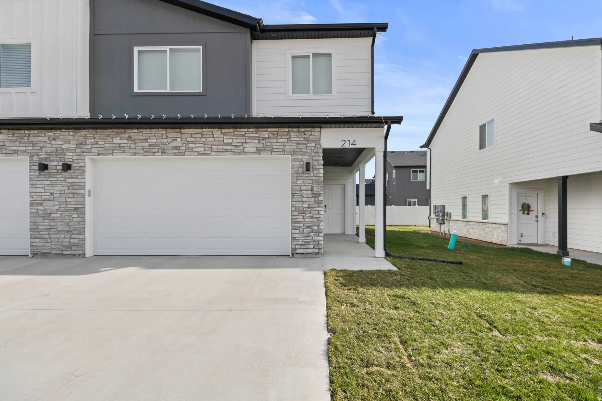 Modern townhome exterior featuring a two-car garage, stone veneer siding, fiber cement paneling, and a covered entryway