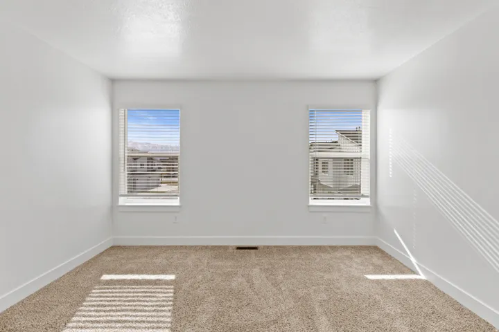 Room featuring neutral-toned carpet, white walls, and two windows with blinds