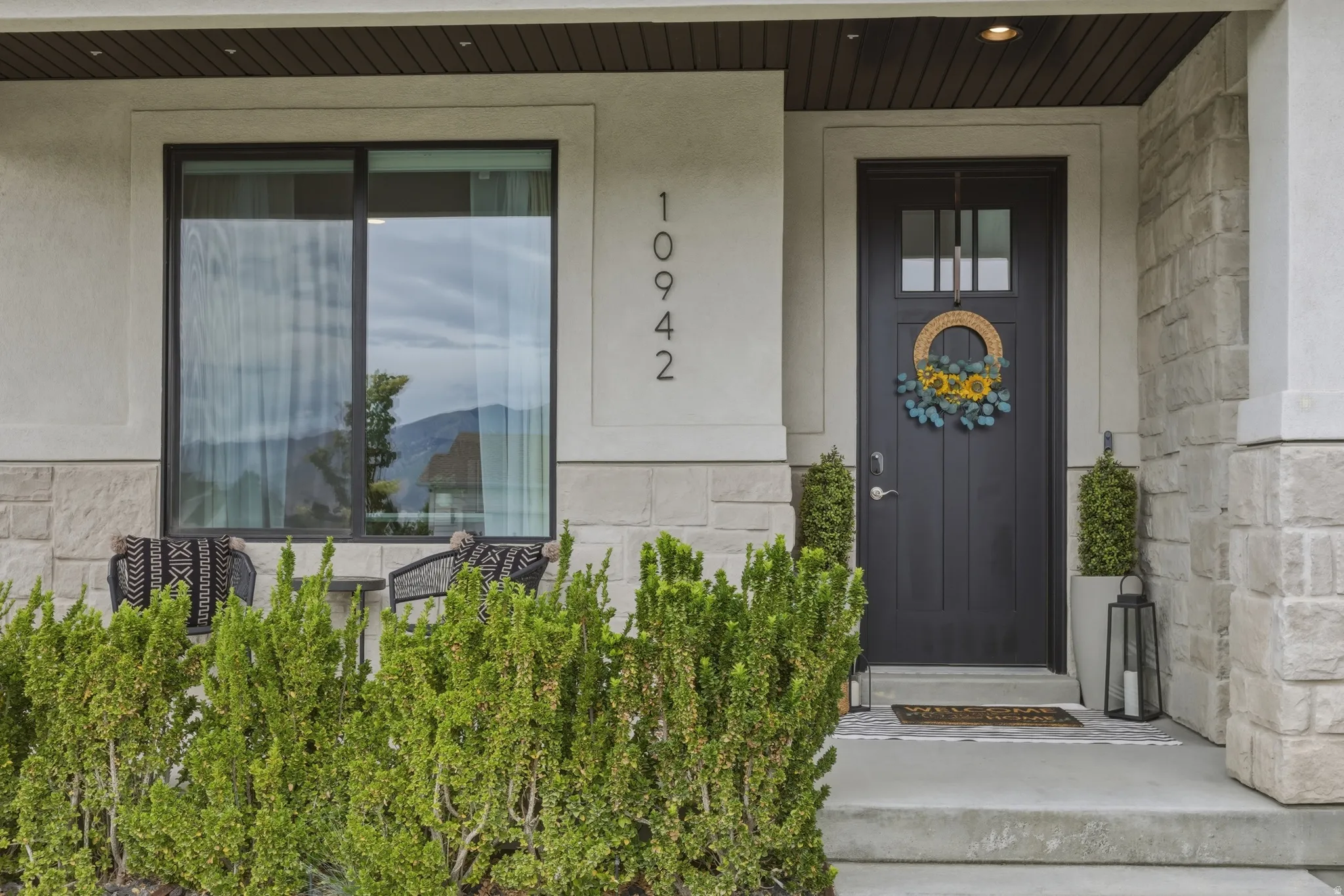 Two-tone exterior with a dark paneled front door, stacked stone siding, and contemporary house numbers
