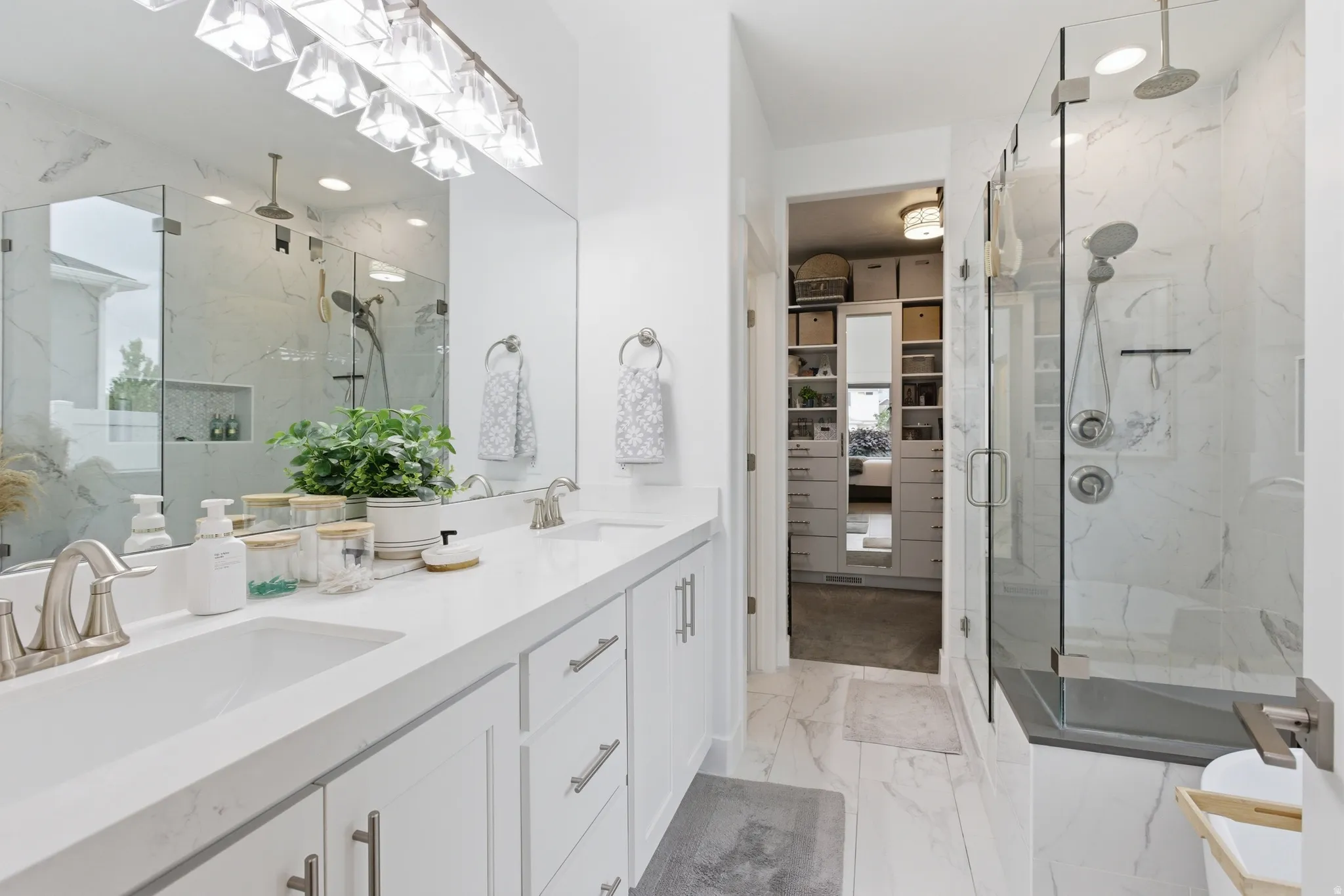 Primary Bathroom featuring a dual vanity with white cabinetry and integrated sinks, a walk-in shower with glass enclosure and rainfall showerhead, and marble-look tile flooring