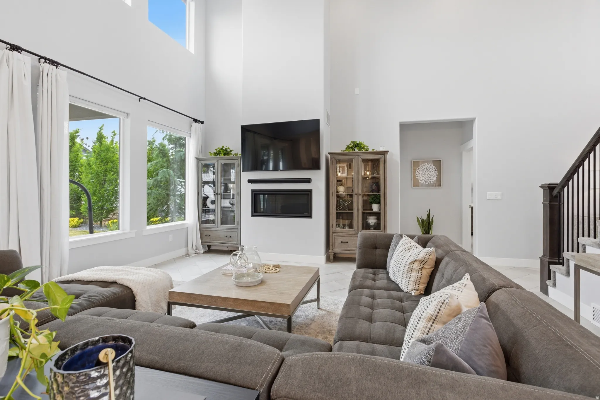 Two-story living area featuring a built-in linear fireplace, high ceilings, large windows, and an open staircase with dark wood newel posts