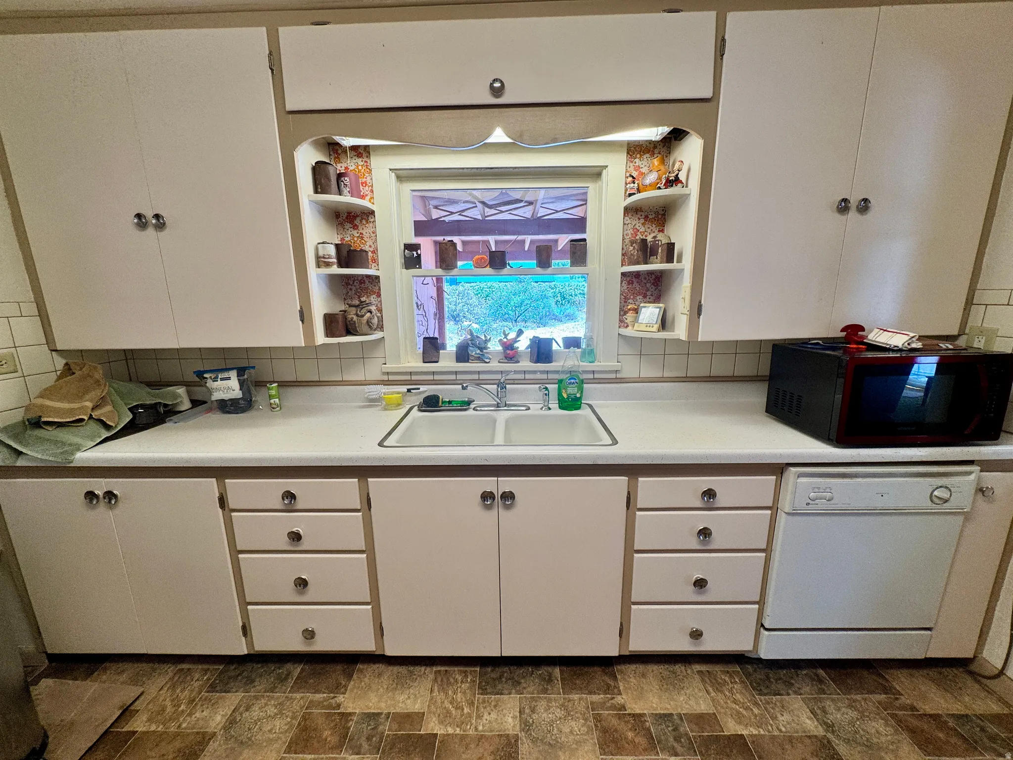 Kitchen area featuring upper and lower cabinetry, a double basin sink, and a built-in dishwasher