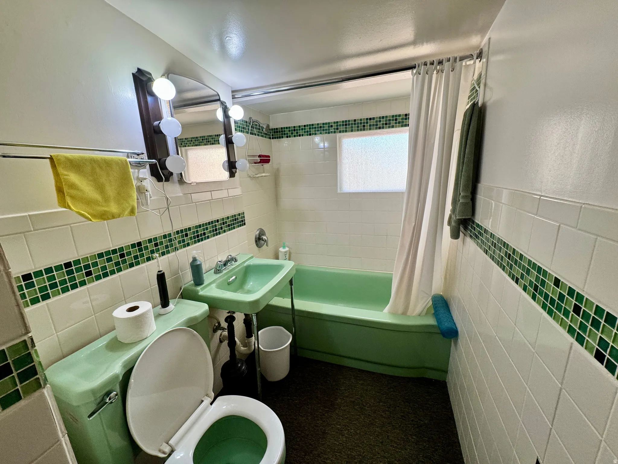 Bathroom featuring white subway tile walls with a decorative green mosaic accent, a green pedestal sink, a green toilet, and a green bathtub with a shower curtain