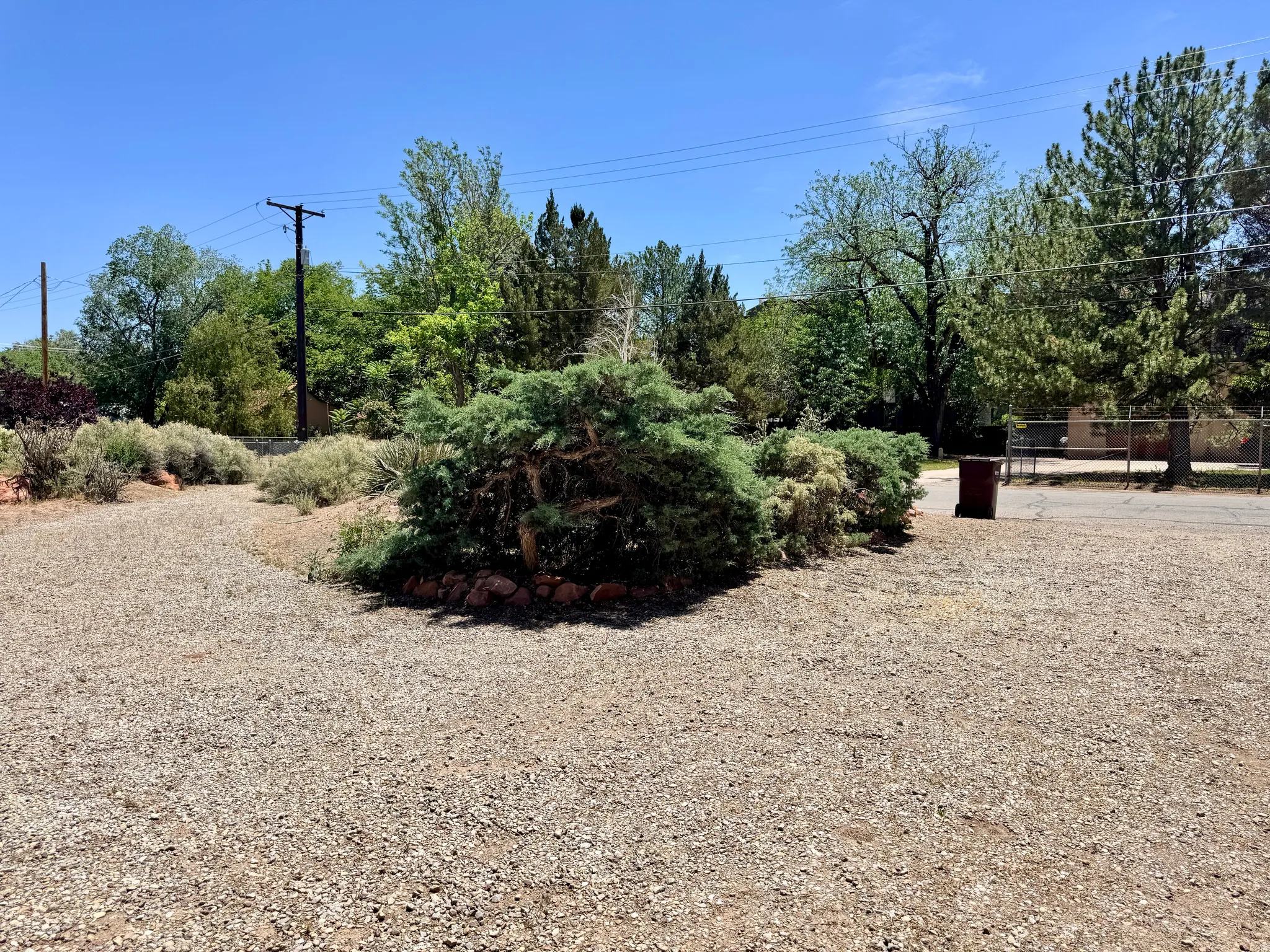 Gravel lot featuring established shrubbery and mature trees