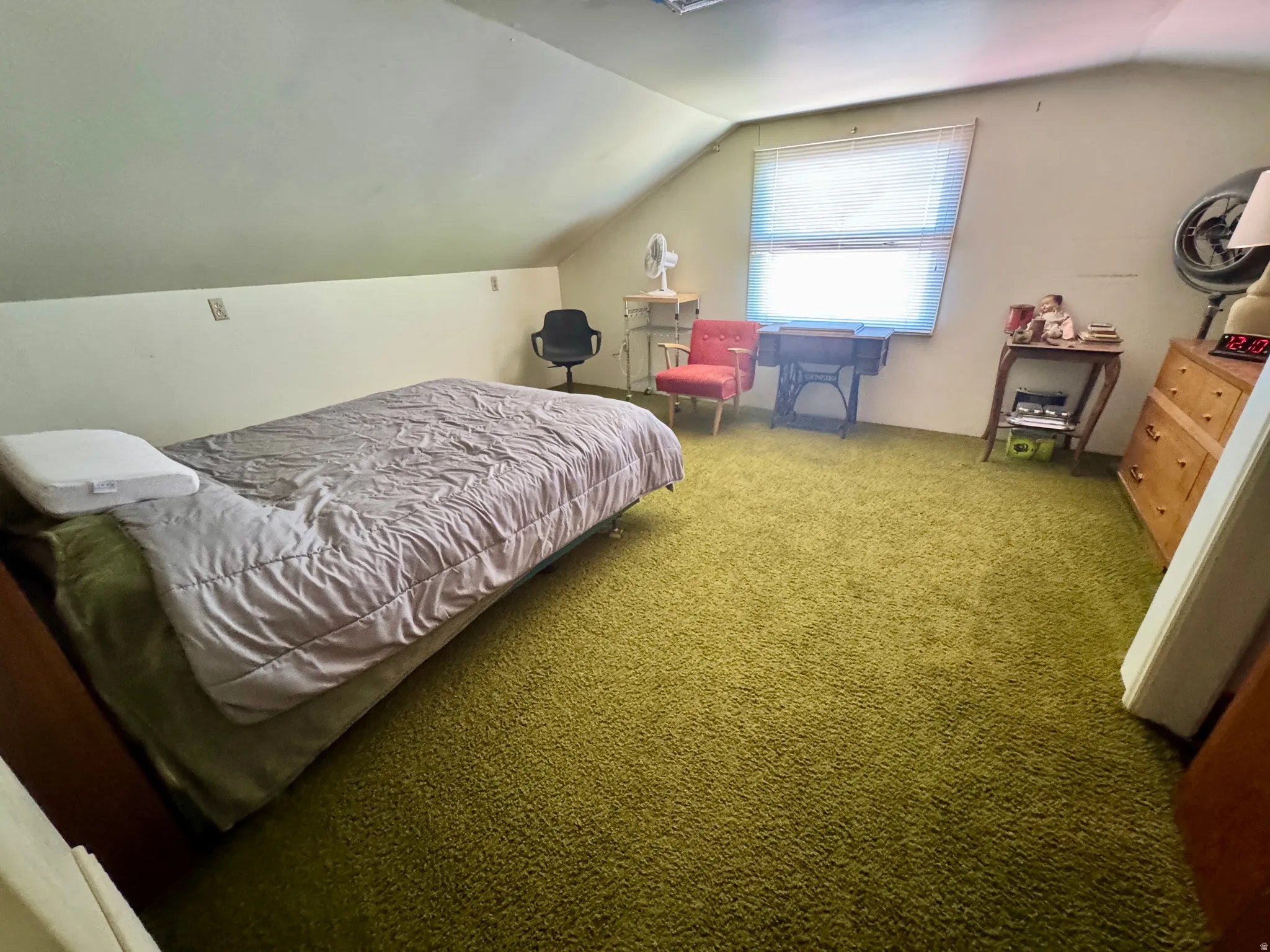 Room with textured green carpeting, sloped ceilings, and a window with blinds