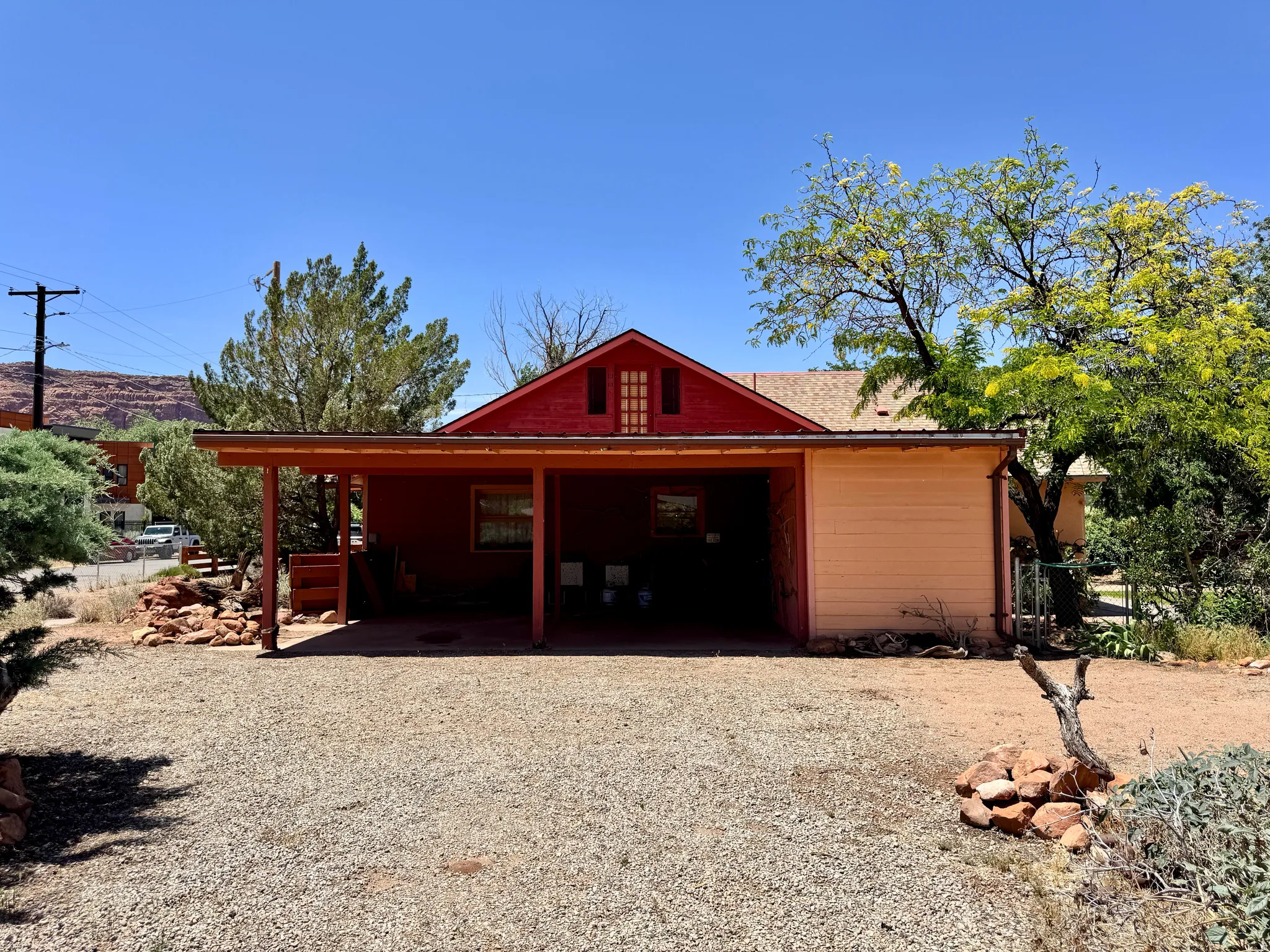 Red-sided residence featuring a covered carport, pitched roof, and a visible attic vent