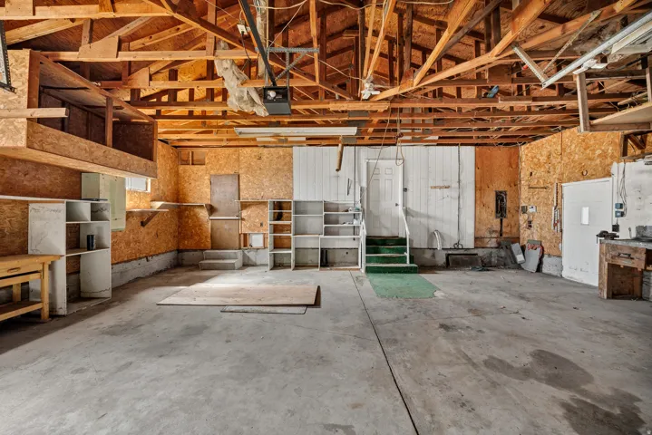 Spacious garage with exposed wood beam ceiling, concrete flooring, built-in shelving, and multiple access doors