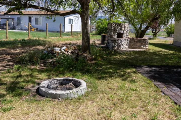 Expansive backyard featuring a stone outdoor oven, a circular stone fire pit, and a dark paver pathway