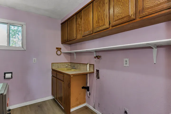Utility space with wood-finish cabinetry, a single basin sink, and a window providing natural light