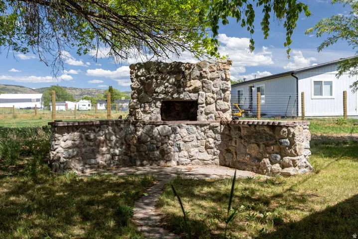 Outdoor stone fireplace with a built-in hearth, surrounded by natural grass and mature trees